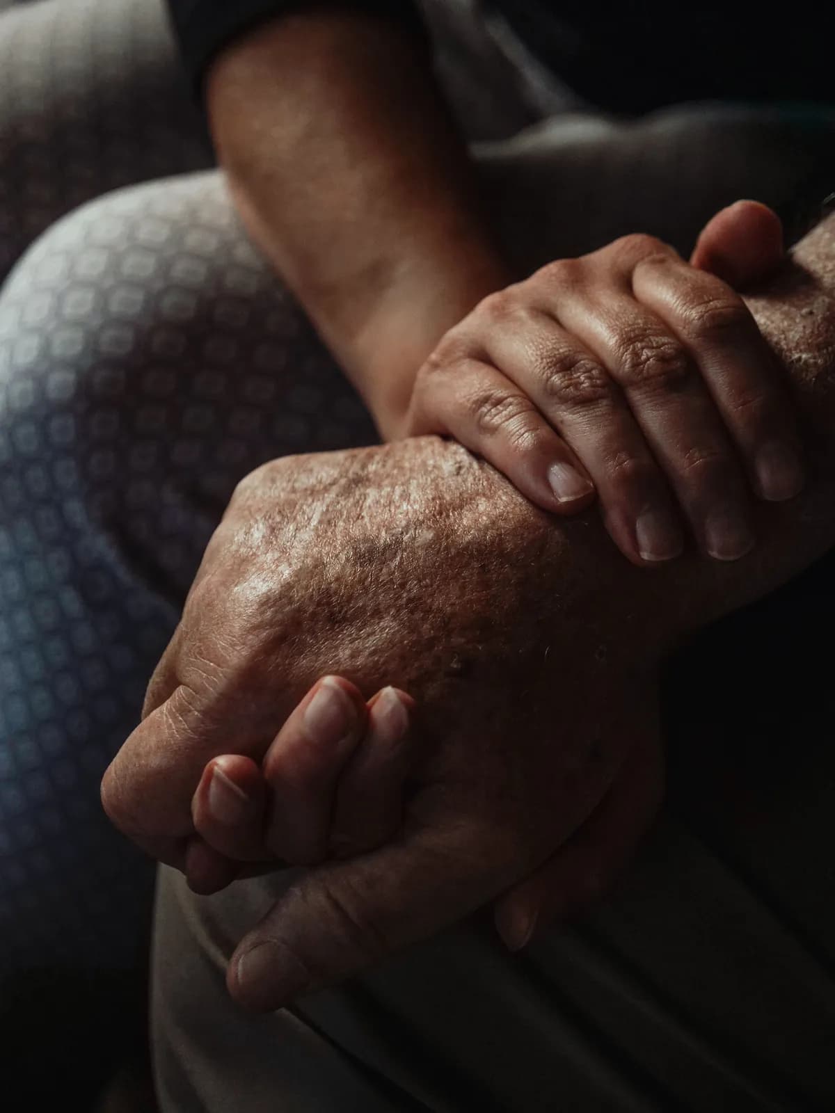 An older person's hands resting on another's arm in a reassuring grip
