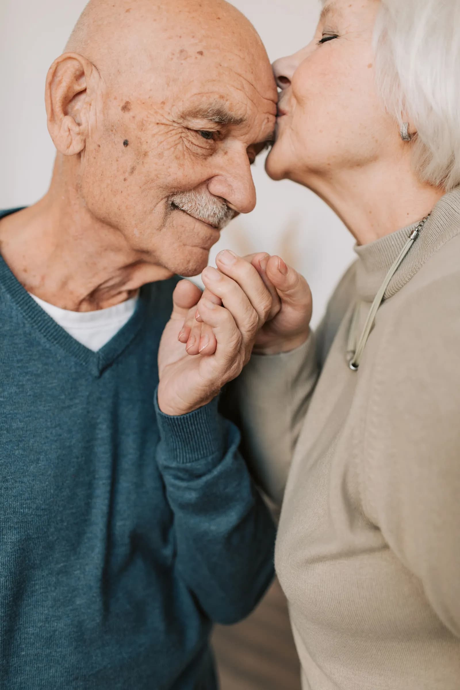 An older woman kisses an older man on the forehead as they hold hands